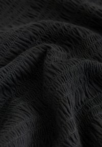 Tissu noir texturé avec un motif ondulé, présentant des coutures surélevées et des variations de volume, créant de la profondeur et un intérêt visuel.