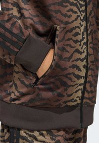 Hnedo-čierna vzorovaná bunda na teplákovú súpravu so zipsovým vreckom, rebrovanými manžetami a textúrovanou tkaninou v dizajne tigrej pruhov.