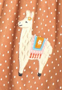 Brauner Stoff mit weißen Punkten, der eine Lama-Stickerei zeigt. Das Lama hat eine Blumenakzent, einen bunten Sattel und eine detaillierte Fellstruktur.