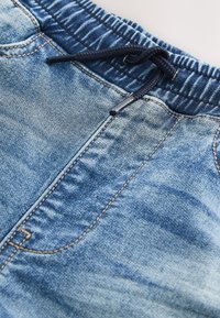 Nahaufnahme von blauer Jeanshose mit elastischem Bund und schwarzem Kordelzug, der locker geknotet ist.