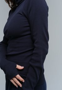Sötétkék bordázott garbó, hosszú ujjakkal, hüvelykujjtartókkal és karcsú szabással, puha textúrájú anyagból készült.