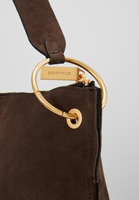 Coin de sac en suède marron avec anneau métallique doré et tirette de fermeture éclair gravée du nom de la marque "COCCINELLE".