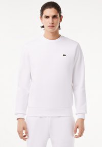 Weißes Sweatshirt aus glattem Stoff, mit Rundhalsausschnitt und gerippten Bündchen, verziert mit einem kleinen grünen Krokodil-Logo auf der Brust.