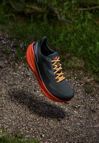 Baskets de course noires avec un dessus texturé, lacets orange et semelle extérieure orange vif, présentant un design épuré et une structure de soutien.