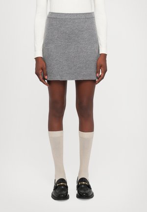 Mini-jupe en laine grise à texture lisse, portée avec des chaussettes montantes crème et des mocassins noirs ornés d'accents en métal doré.