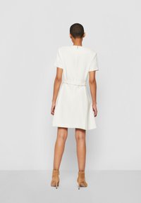 Korte mouwen, getailleerde witte jurk met een ceintuur in de taille en een rits aan de achterkant, gemaakt van een gladde stof met een vloeiende rok.