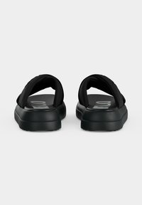 Ζευγάρι μαύρα σανδάλια τύπου slip-on με παχιά επενδυμένα λουριά και χοντρές σόλες, από πίσω σε λευκό φόντο.