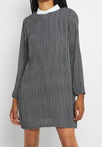 Svart och vit mönstrad klänning med långa ärmar, rund halsringning och en kontrastfärgade vit krage, med en avslappnad passform och textilstruktur.