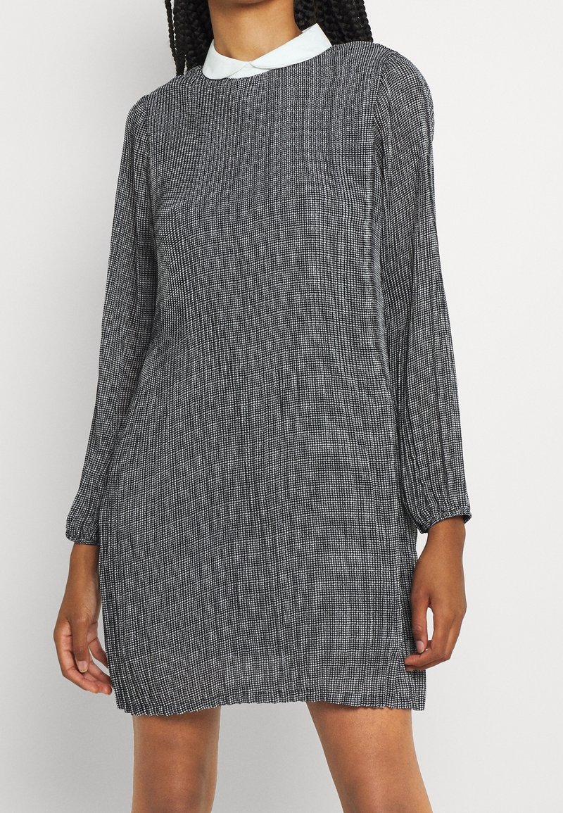 Svart och vit mönstrad klänning med långa ärmar, rund halsringning och en kontrastfärgade vit krage, med en avslappnad passform och textilstruktur.