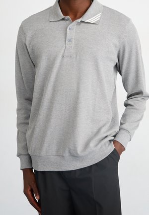 Graues Polohemd mit langen Ärmeln, texturierter Stoff, Drei-Knopf-Leiste und kontrastierenden weißen Streifen am Kragen. Dezentes Branding sichtbar.