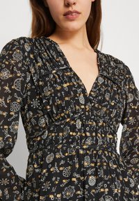 Vestido preto texturizado com um design plissado, decote em V profundo e um padrão floral em detalhes brancos e dourados. Inclui mangas longas.