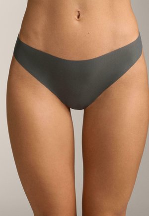 Sezione centrale del corpo di una donna che indossa mutandine senza cuciture di colore grigio stile bikini su uno sfondo neutro e uniforme.