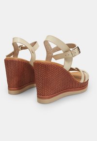 Sandali con tacco a cuneo in pelle beige, caratterizzati da un tacco in sughero intrecciato di colore marrone rossiccio con una finitura texturizzata e cinturini alla caviglia regolabili.