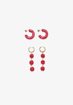 Due paia di orecchini su sfondo bianco; un paio di cerchi rossi traslucidi, l'altro paio di cerchi dorati con tre ciondoli a forma di pomodoro rosso appesi ciascuno.