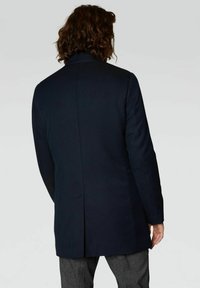 Abrigo azul marino con un diseño estructurado, que cuenta con una abertura trasera, mangas largas y una textura suave. La tela parece gruesa y confeccionada a medida.