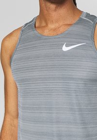 Gray sleeveless athletic tank top with horizontal texture, featuring a white Nike logo on the chest. Nylon blend fabric with minimal seams.