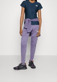 Laivaston sininen t-paita, violetit joggersit teksturoidulla kankaalla ja mustat urheilukengät punaisilla ja vaaleanpunaisilla yksityiskohdilla. Logot sekä paidassa että housuissa.