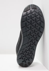 Suola nera di una scarpa sportiva con una suola in gomma testurizzata e un motivo di battistrada geometrico, che migliora la presa e la durabilità.