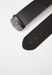 Black leather strap with a smooth texture, featuring a rounded end, adjustment holes, and a decorative gold stud on the end tab.