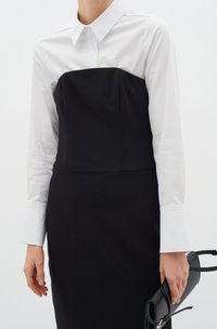 Rochie structurată neagră cu overlay din cămașă albă cu guler. Prezintă mâneci lungi și o textură netedă, completată de un accesoriu negru.