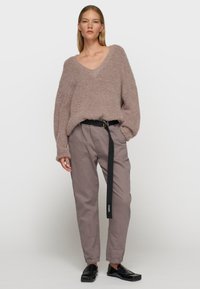 Przesadnie duży, puszysty sweter w odcieniu mauve, luźny krój, dekolt w serek, zestawiony z jasnoszarymi spodniami z czarnym paskiem z logo. Czarne buty wsuwane.
