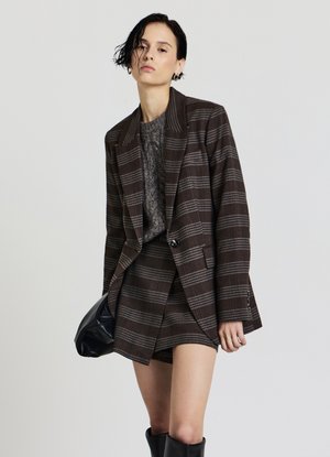 Blazer a quadri marrone con strisce grigie, abbinato a un maglione grigio testurizzato e una gonna corta coordinata, completato da stivali neri al ginocchio.