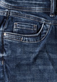 Pantalones vaqueros de mezclilla en un tono azul oscuro, con un bolsillo trasero, costuras amarillas en contraste y un acabado suave y texturizado.