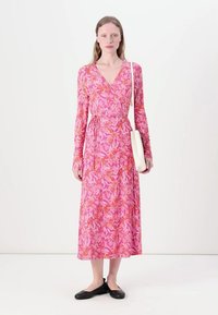 Rochie cu mânecă lungă, stil înfășurat, cu un model floral în nuanțe de roz, portocaliu și liliac. Are talie legată și fustă fluidă, asortată cu o geantă albă.