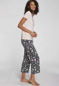 Lichtroze t-shirt met korte mouwen en decoratieve tekst, gecombineerd met donkere broek met een bloemenpatroon, cropped pijpen en zachte stof.