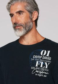 Navyblauwe katoenen T-shirt met witte en blauwe bedrukte tekst, waaronder "01 CAMP DAVID" en een grafisch ontwerp van een spinnakerzeil.