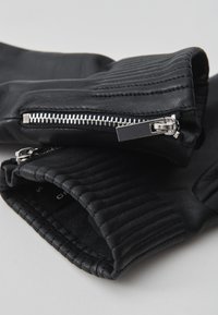 Schwarze Lederhandschuhe mit einer gerippten Textur am Handgelenk und silbernen Reißverschlüssen auf beiden Seiten, insgesamt mit einer glatten Oberfläche.