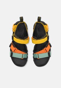 Sandalias negras con correas ajustables en amarillo, naranja y verde. Incluyen una plantilla acolchada y una suela de goma texturizada para mayor agarre.