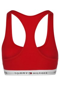 Reggiseno sportivo rosso con design a schiena scoperta. Realizzato in tessuto morbido, presenta un elastico bianco nella parte inferiore con la scritta "TOMMY HILFIGER" stampata.