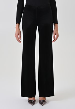 Pantaloni ampi in velluto nero con una texture liscia, vita alta e lunghezza fino al pavimento. Abbinati a décolleté a punta con fiocco.