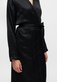 Gros plan sur une personne portant une robe portefeuille noire avec un motif à carreaux subtil et une ceinture nouée à la taille.