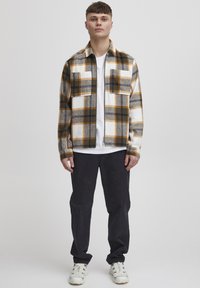 Flannel shirt with a checkered pattern in shades of orange, white, and earthy tones; features two chest pockets and a collared design.
