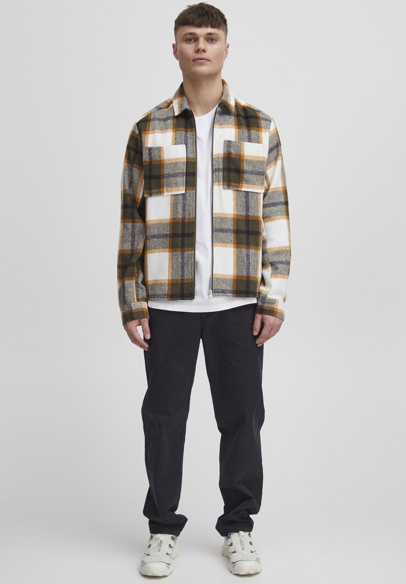 Flannel shirt with a checkered pattern in shades of orange, white, and earthy tones; features two chest pockets and a collared design.