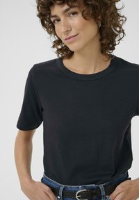 T-shirt noir à manches courtes avec un col rond, texture lisse et silhouette ajustée, accompagné d'une ceinture en denim bleu.