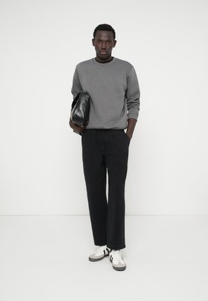 Gray sweatshirt, black loose-fitting pants, and white sneakers with black accents; holding a small black bag. Simple design, neutral colors.