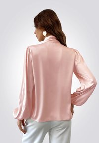 Blusa de satén rosa claro con un cuello alto, mangas largas abullonadas y una textura suave, con un corte holgado y una caída suave.