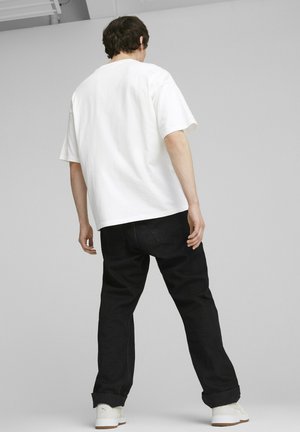 T-shirt bianco in cotone con una vestibilità comoda, abbinata a jeans in denim neri. I jeans sono leggermente arrotolati ai polsini e presentano tasche posteriori.