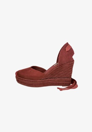 Alpargata de cuña roja con puntera cerrada, plataforma trenzada de yute y lazo para atar en el tobillo, con contrafuerte tejido en el talón.