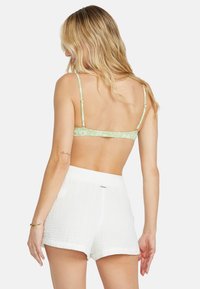 Vihreä kukkakuosiset bralette, jossa on ohutolkaimet, yhdistetty valkoisiin teksturoituihin shortseihin, joissa on joustava vyötärö ja käännetyt lahkeet.