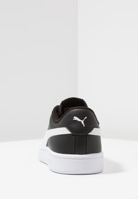 Černobílé tenisky Puma z pohledu zezadu, ukazující logo Puma na patě a bílou podrážku na bílém pozadí.