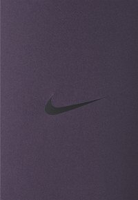 Fioletowa tkanina sportowa charakteryzuje się gładką teksturą i subtelnym połyskiem. Na materiale znajduje się wyraźnie umieszczone czarne logo Nike w kształcie półksiężyca.