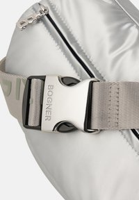Sølv nylon bæltetaske med en sort og sølv spænde. Har en lynlås og grå rem, hvilket fremhæver det slanke design og den glatte tekstur.
