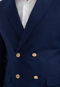 Blazer double boutonnage bleu marine avec des boutons dorés, un col cranté et une poche poitrine, fabriqué en tissu lisse avec une coupe ajustée.