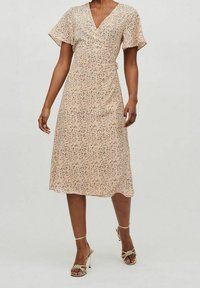 Kukkakuvioinen kietaisumekko pehmeästä persikanvärisestä kankaasta, jossa on lyhyet liehukkeet hihansuut ja midipituiset hameen helmat, täydentää metallikorkoiset sandaalit.