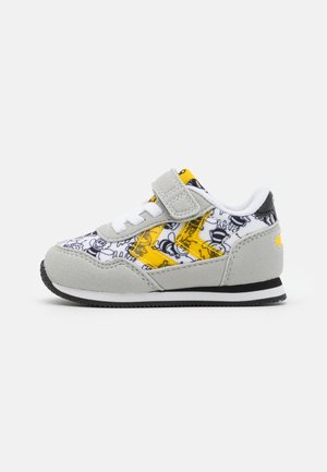 Børnesneaker med gråt ruskind, hvidt stof med sorte tegneserieansigter og gule chevronstriber, med hvide snørebånd og velcrolukning.