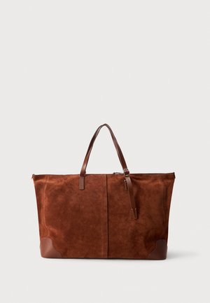 Grand sac cabas en daim marron, avec de longues anses en cuir pour le porter à l’épaule et des empiècements en cuir aux coins, sur un fond clair uni.